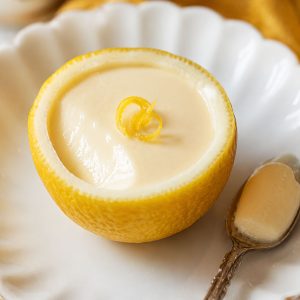 Close-up of a single easy lemon posset in a lemon shell on a white plate with a vintage silver spoon
