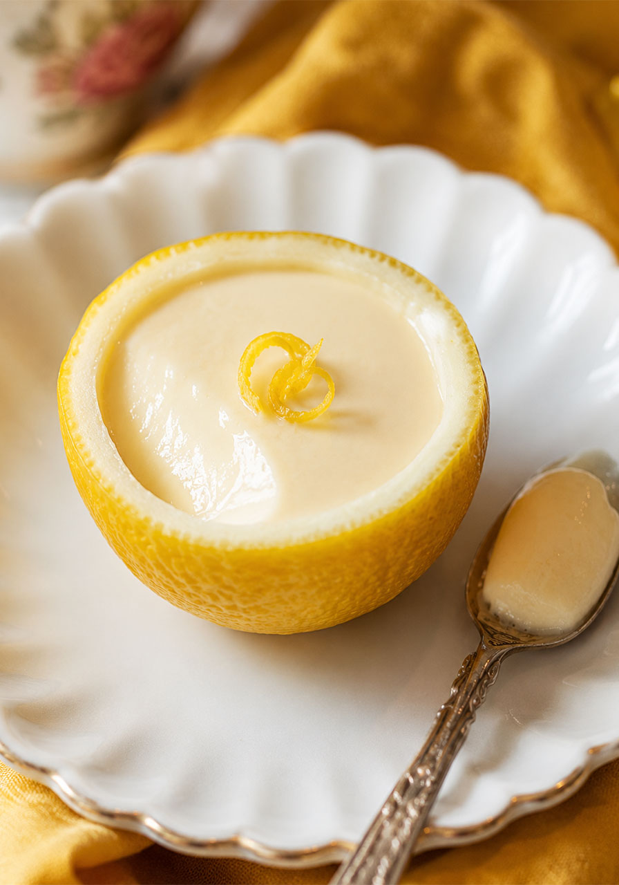 Close-up of a single easy lemon posset in a lemon shell on a white plate with a vintage silver spoon