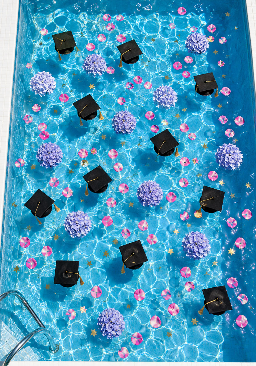 Miniature black graduation caps and rose petals floating in a swimming pool for a creative graduation pool party decoration