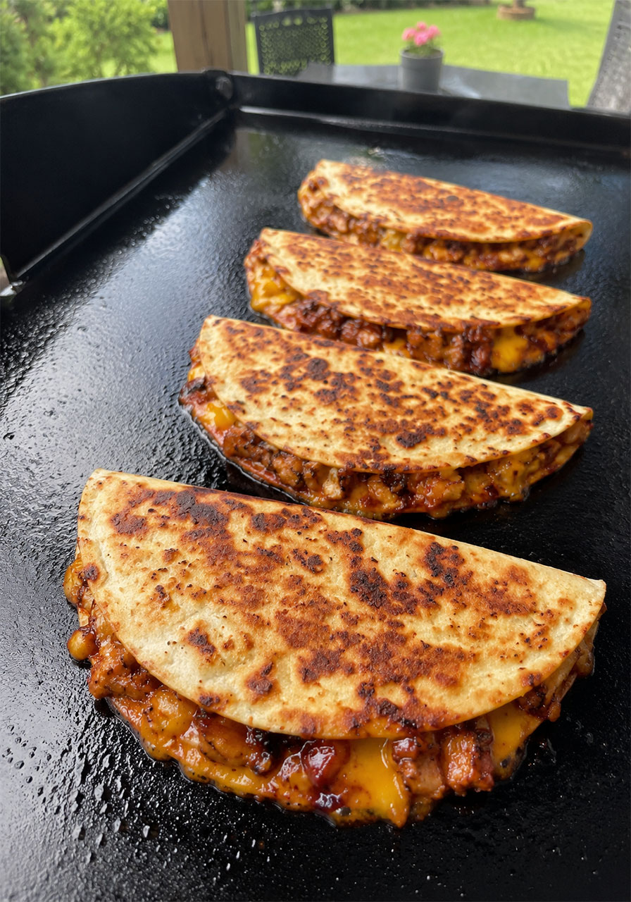 Four folded hot honey BBQ chicken quesadillas crisping on Blackstone flat top griddle with golden caramelized tortillas
