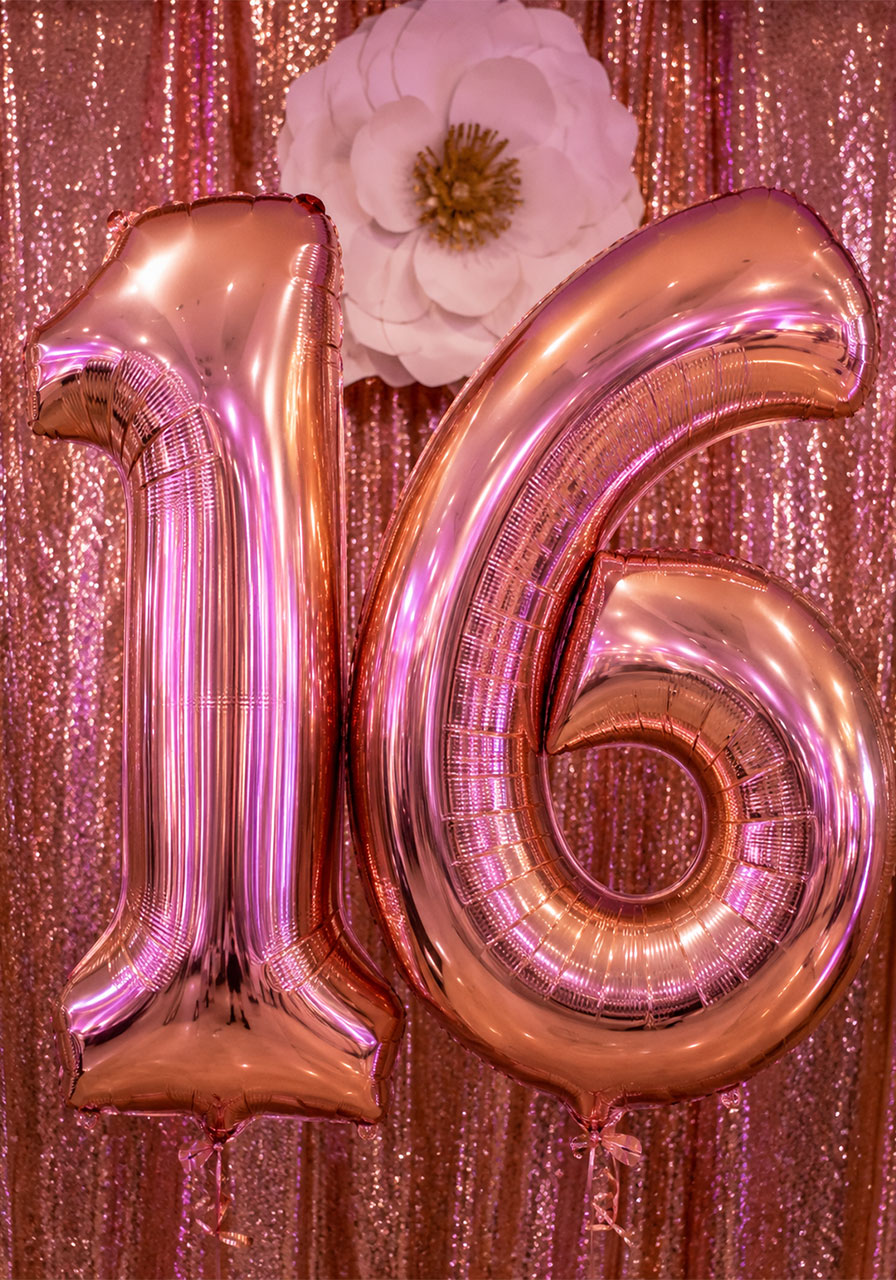 Giant rose gold foil number 16 balloons in front of a sequin backdrop for a Sweet 16 birthday party photo booth