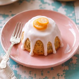 Single glazed mini lemon poppyseed tea cake with citrus glaze dripping down the sides on a pink plate