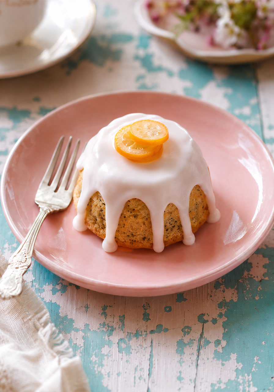 Single glazed mini lemon poppyseed tea cake with citrus glaze dripping down the sides on a pink plate