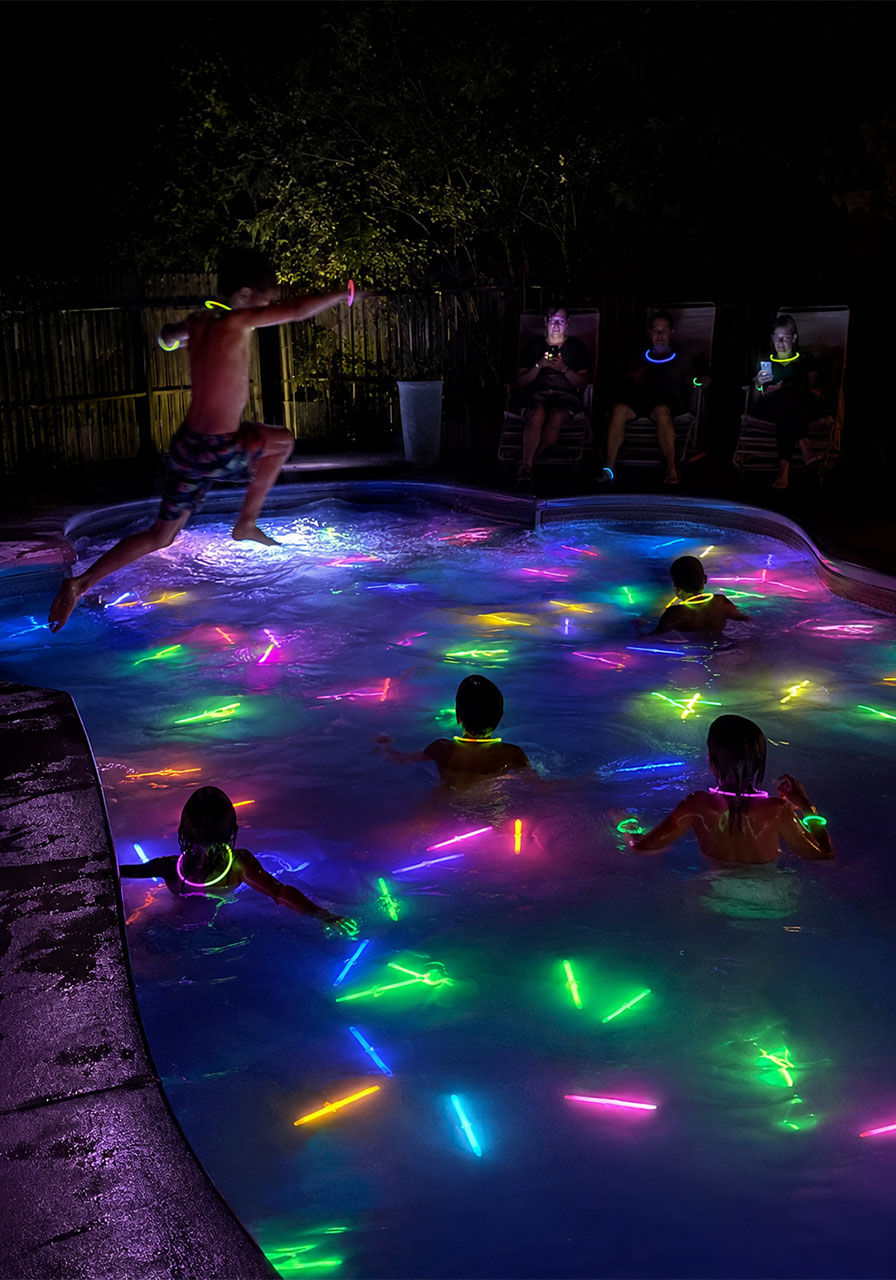 Backyard pool glowing with neon glow sticks and glow bracelets for a magical night swim at a summer pool party