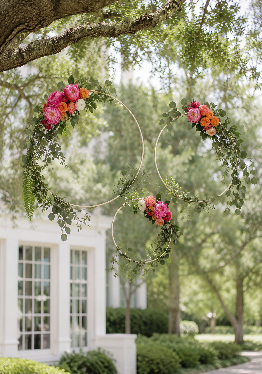 Three gold embroidery hoops wrapped with eucalyptus, peonies, and roses hanging at outdoor garden bridal shower