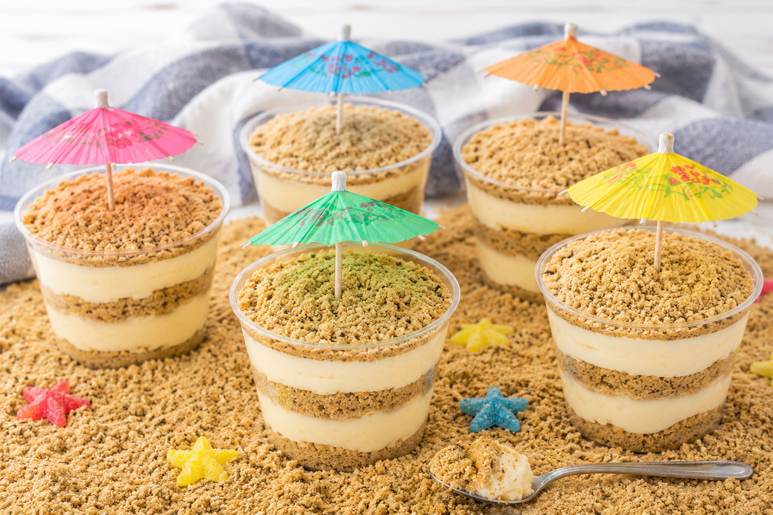 Five cups of Golden Oreo Sand Pudding topped with colorful umbrellas for a beach party