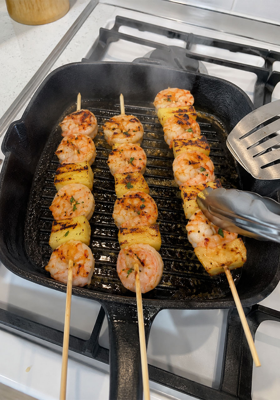 Pineapple shrimp skewers cooking in a cast iron grill pan on an indoor stovetop as a no-grill alternative method