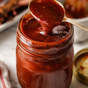 Homemade BBQ sauce in a glass mason jar with a spoon dripping thick glossy sauce