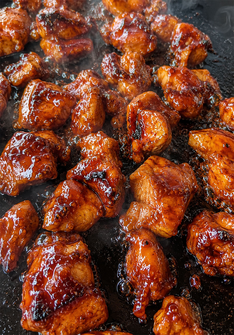 Close-up of sticky caramelized hot honey BBQ chicken bites cooked on Blackstone flat top griddle