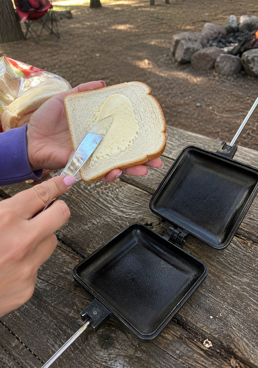 Spreading butter on white bread before placing it in a campfire pie iron to make a strawberry pudgy pie