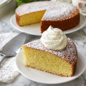 A slice of Irish tea cake dusted with powdered sugar and topped with whipped cream on a white plate