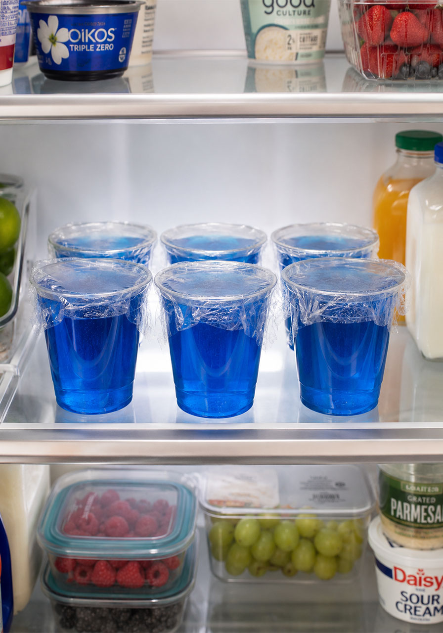 Six Blue Jello cups covered with plastic wrap and stored overnight in the refrigerator – make-ahead tip for pool party dessert prep