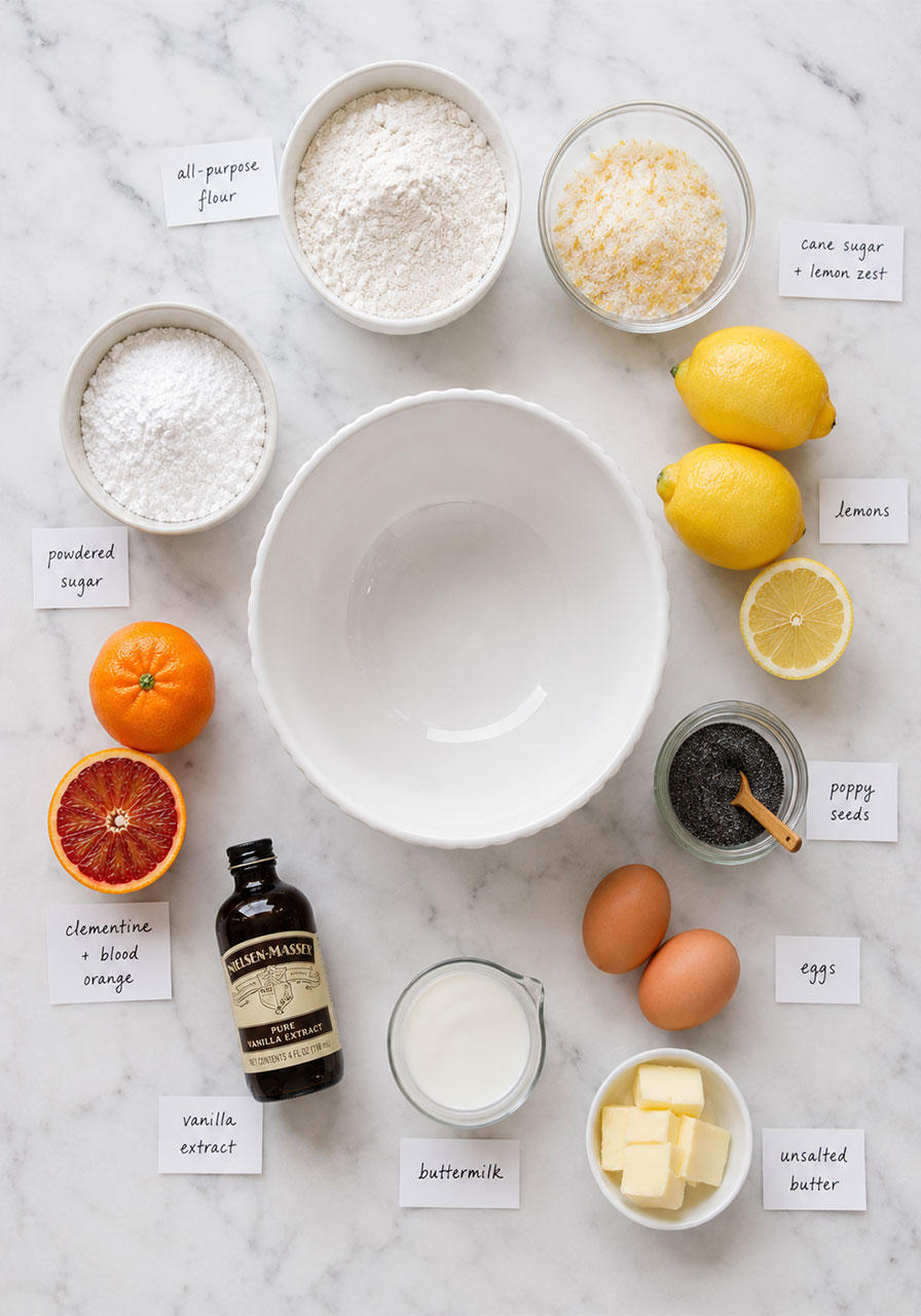 All ingredients for glazed mini lemon poppyseed tea cakes laid out in a flat lay including lemons, poppy seeds, buttermilk, and blood orange