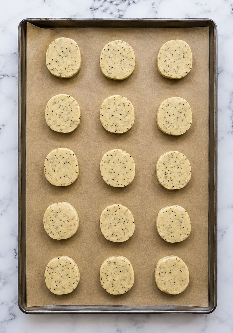Unbaked London Fog cookie slices arranged on a parchment-lined baking sheet