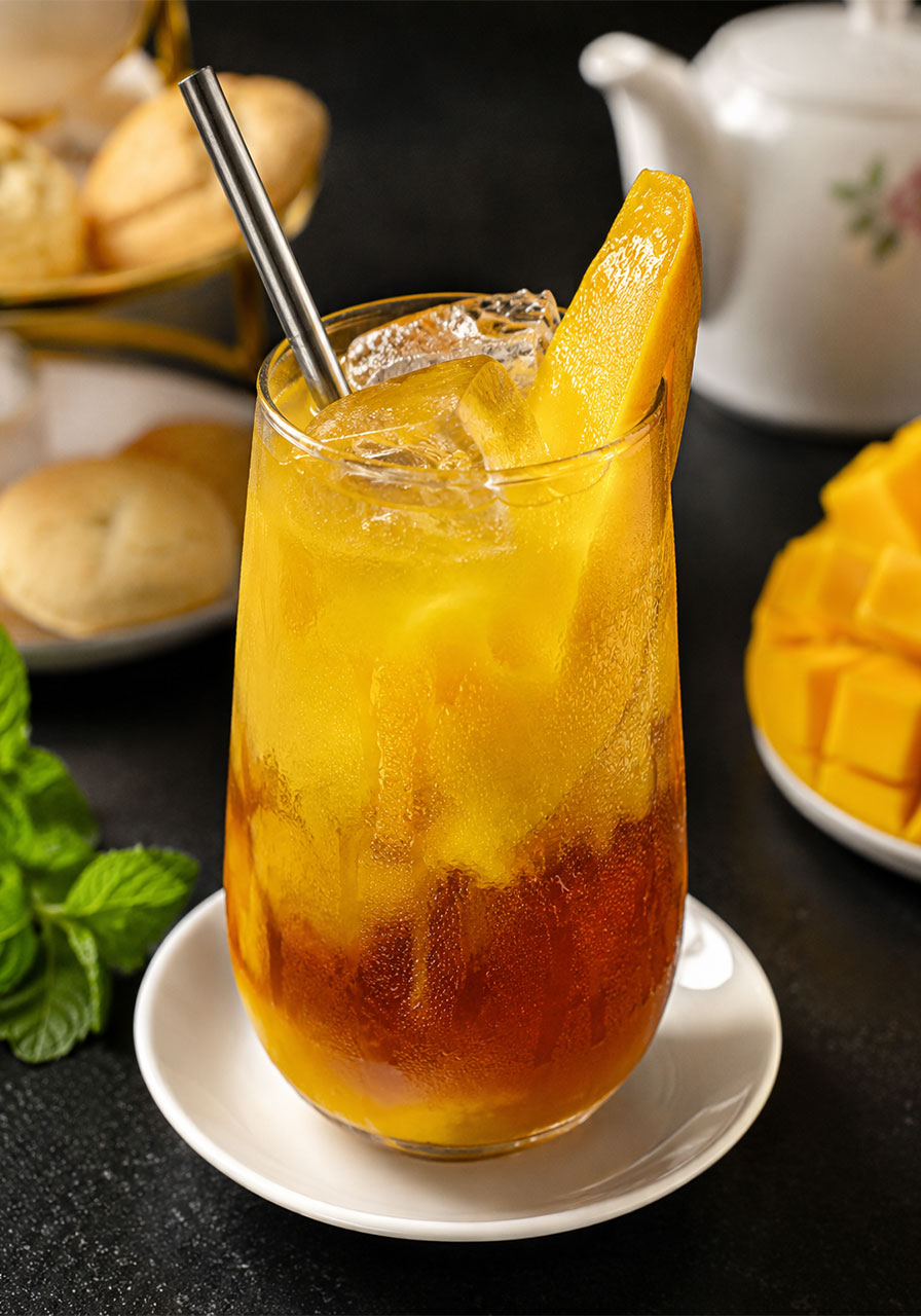 Homemade mango iced tea recipe with beautiful golden layered effect in a clear glass with ice and mango garnish