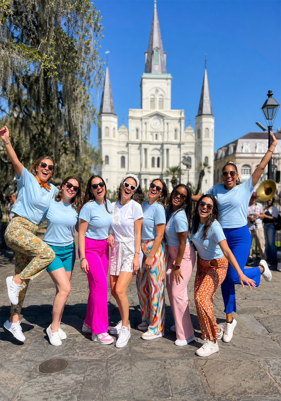 Bachelorette party group in matching shirts jumping in front of Saint Louis Cathedral in New Orleans French Quarter
