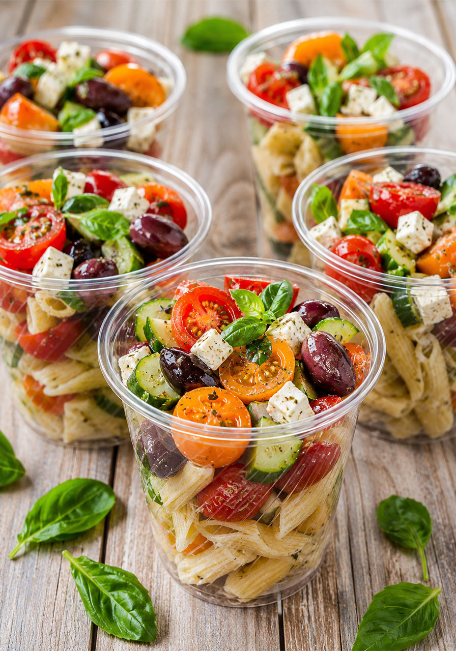 Individual pasta salad cups with cherry tomatoes, feta, olives, and basil in clear serving cups for a bridal shower buffet