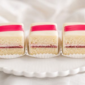 Close-up of perfect petit fours recipe showing golden cake layers with raspberry filling and white chocolate glaze