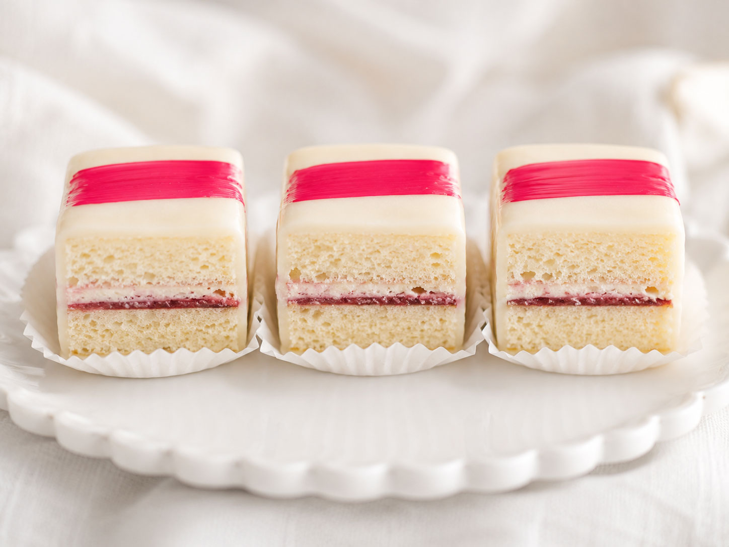 Close-up of perfect petit fours recipe showing golden cake layers with raspberry filling and white chocolate glaze