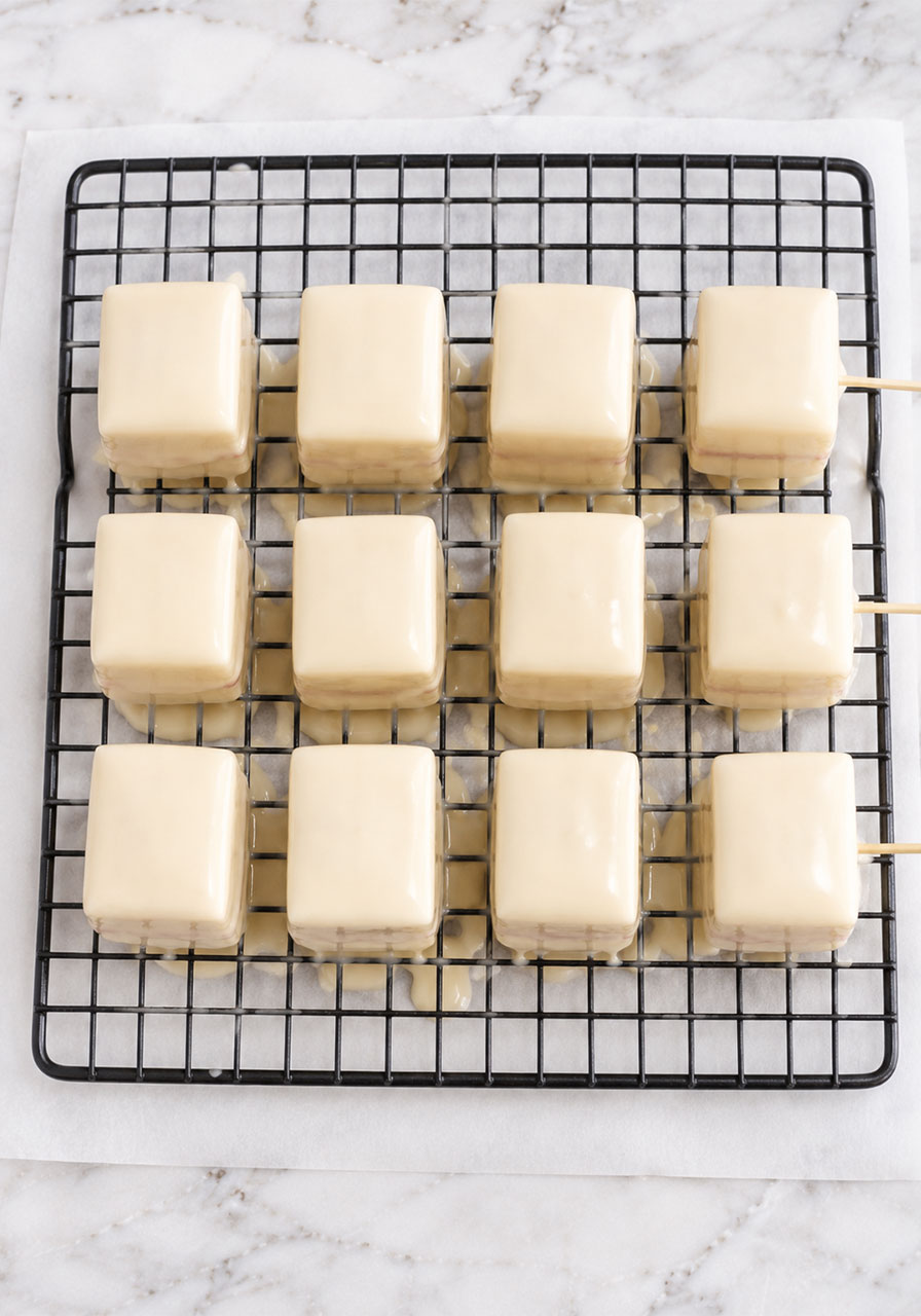 Freshly iced petit fours with white chocolate glaze setting on wire cooling rack after dipping