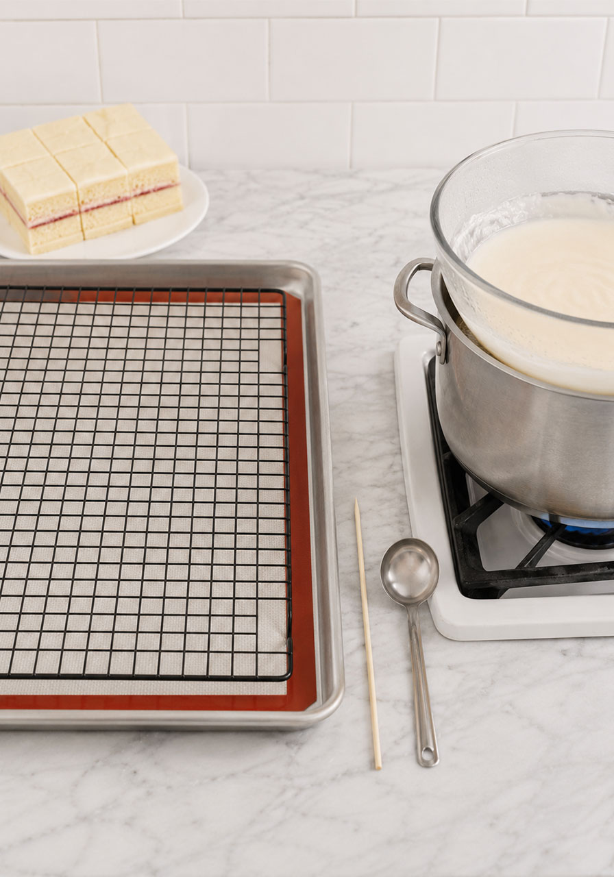 Complete petit fours icing station setup with cooling rack over lined sheet pan and warm glaze ready