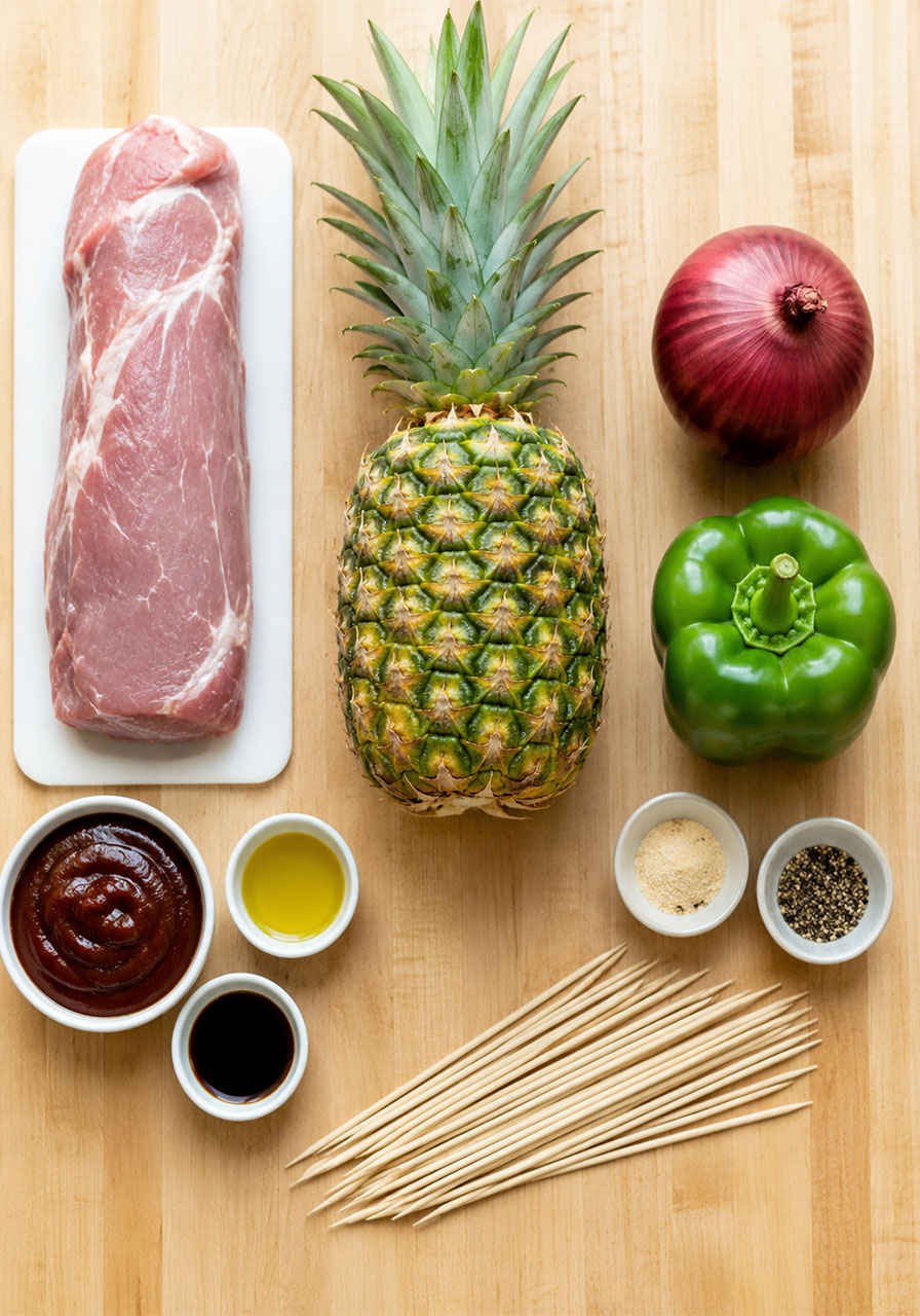 All fresh ingredients for pineapple BBQ pork skewers laid out including pork tenderloin, fresh pineapple, red onion, bell pepper and BBQ marinade