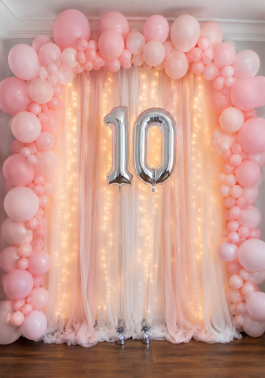 Pink balloon arch framing a sheer fabric fairy light curtain backdrop with silver number 10 balloons for a 10th birthday photo booth