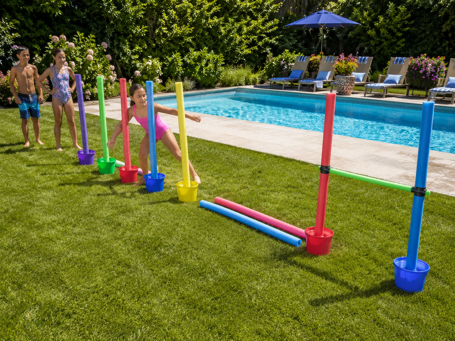 DIY pool noodle obstacle course with weave poles, balance beam, and limbo bar set up in a backyard for a pool party activity