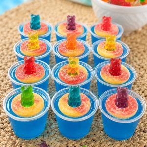 Finished pool party jello shots on a tray, topped with peach ring gummies and gummy bears