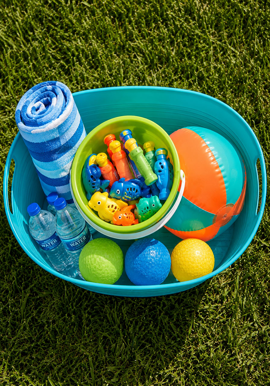Bird's eye view of teal party favor tub filled with beach ball, towel, water toys and mini bottles for kids pool party