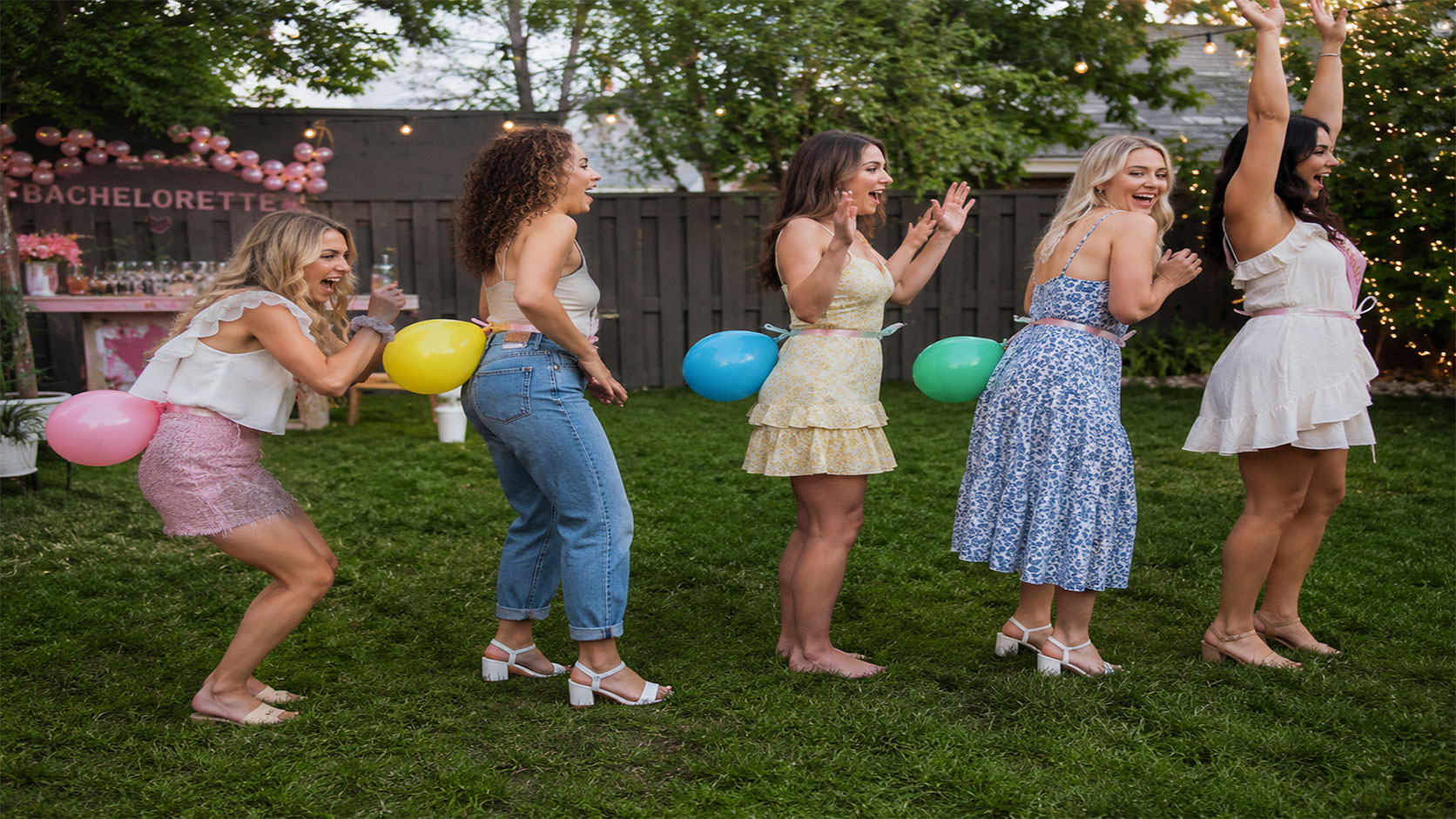 Women playing the pop the balloon relay race game at a bachelorette party outdoors