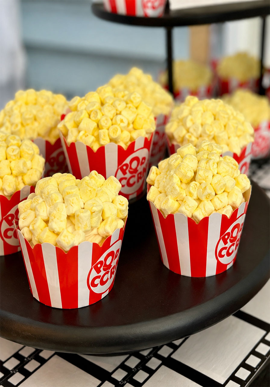 Popcorn cupcakes with yellow marshmallow topping in red and white striped holders for a movie theater birthday party