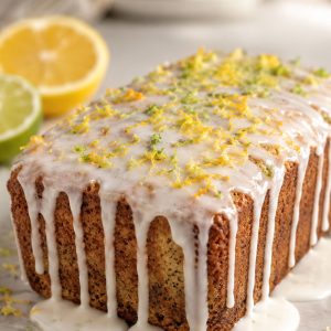 Poppyseed citrus tea cake with double citrus glaze dripping down the sides, garnished with lemon and lime zest