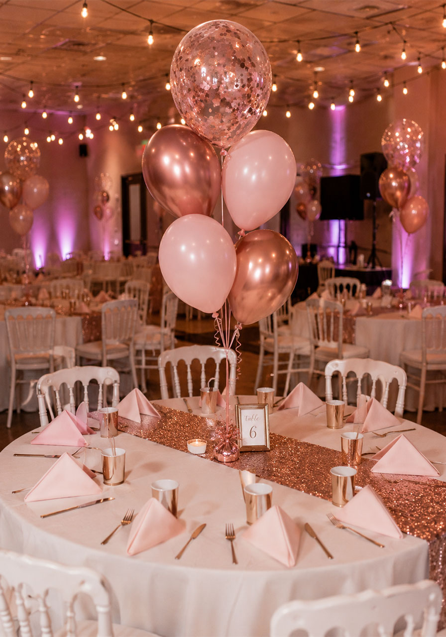 Rose gold and pink balloon bouquet centerpiece floating above a round guest table at a Sweet 16 birthday party