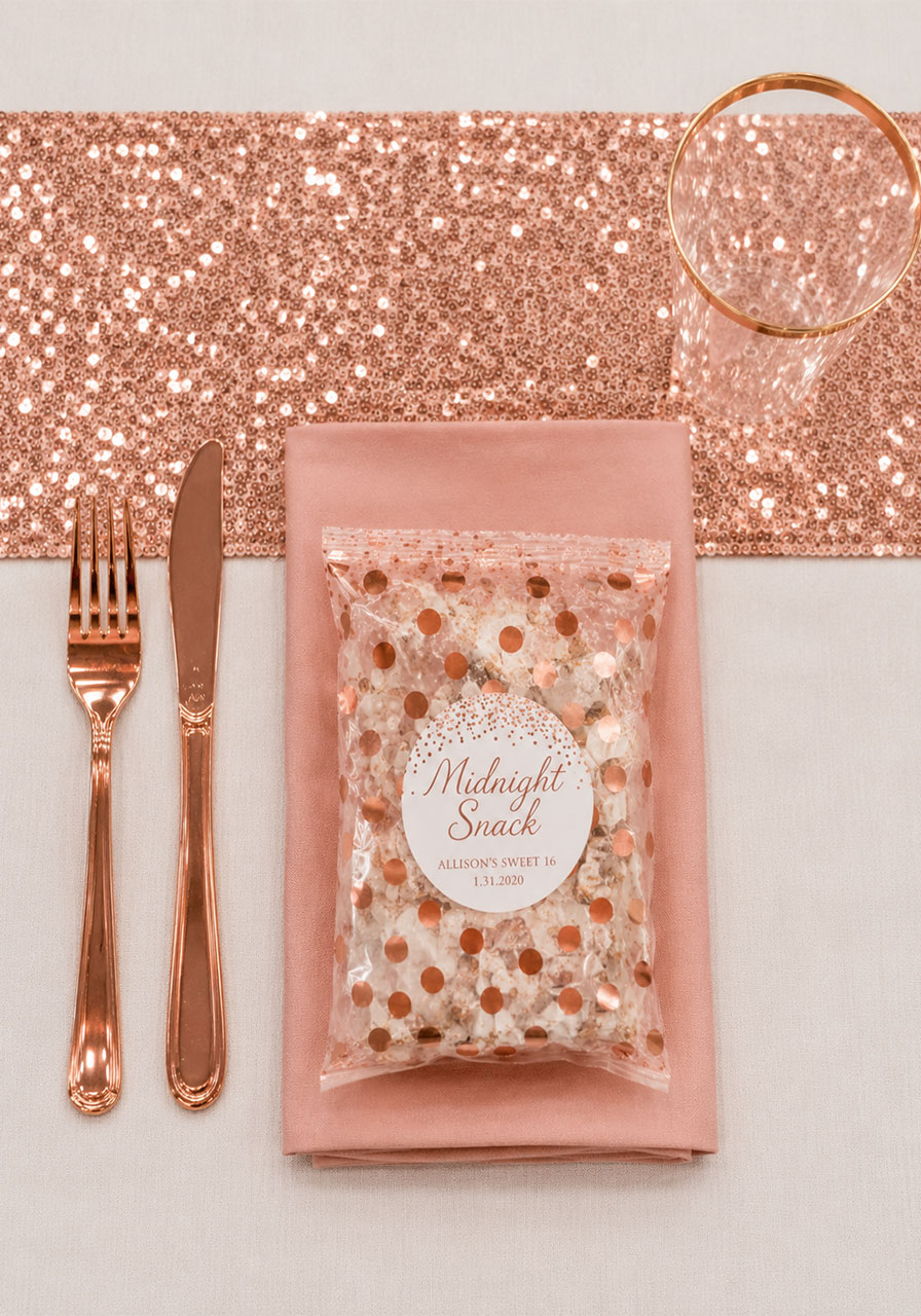 Rose gold place setting with sequin runner, blush napkin, metallic cutlery, and personalized favor bag for a Sweet 16