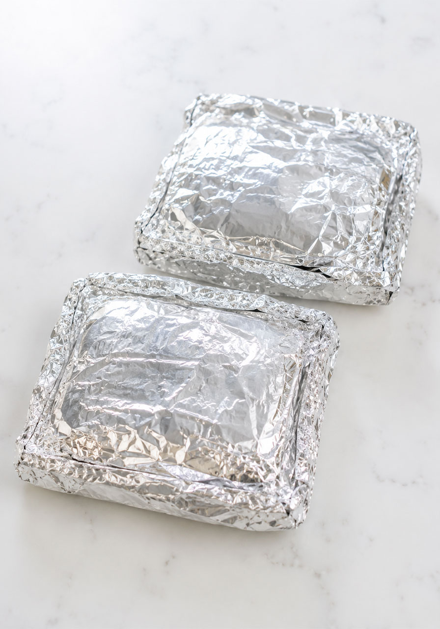 Two tightly sealed double-wrapped aluminum foil packets for campfire apple pie packets ready for the grill or campfire