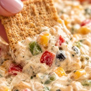 Close-up of a Wheat Thins cracker scooping a generous portion of skinny poolside dip showing creamy texture with vegetables