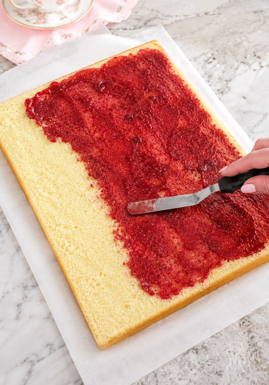 Spreading a thin layer of raspberry filling on bottom cake layer for petit fours assembly