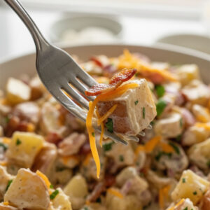 Close-up of a fork lifting a creamy bite of steakhouse potato salad with bacon, cheddar, and Dijon dressing
