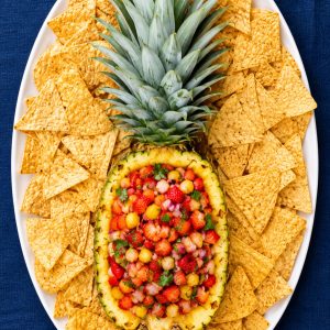 Overhead view of strawberry pineapple salsa in a pineapple bowl surrounded by tortilla chips on a serving platter