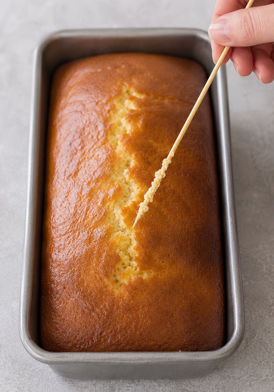 Skewer test showing moist honey tea cake loaf is fully baked
