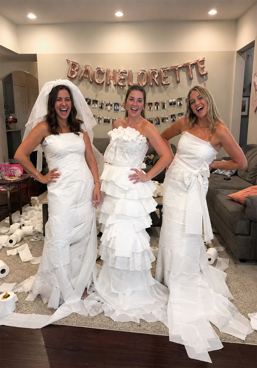 Women modeling toilet paper wedding dresses at a bachelorette party game challenge