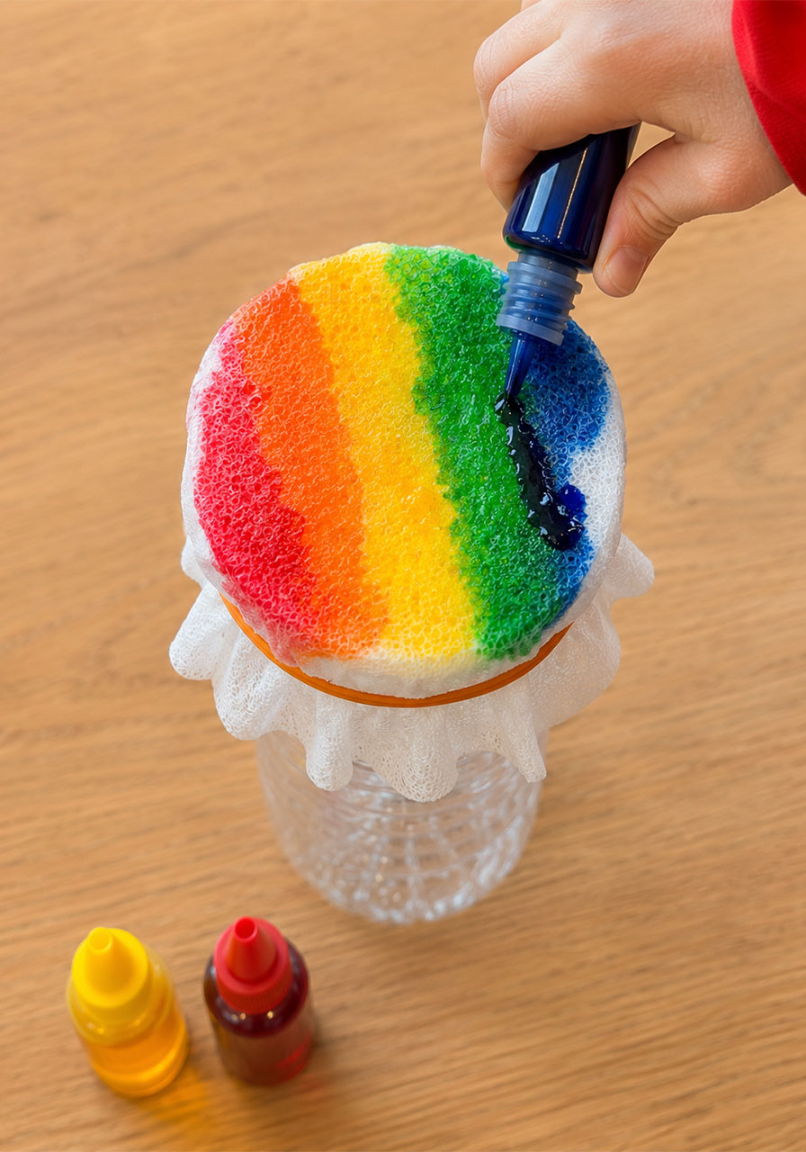 Adding rainbow food coloring to fabric-covered bottle for bubble snake STEM activity