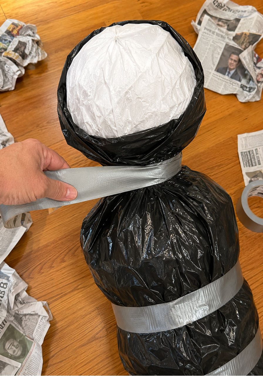 Taping the neck of a bagged Halloween body prop to attach the head