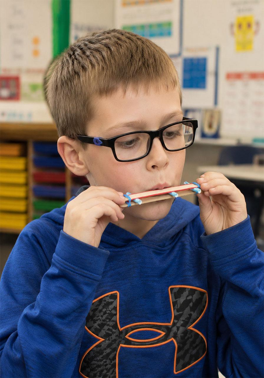 Child blowing into a craft stick harmonica to make sound