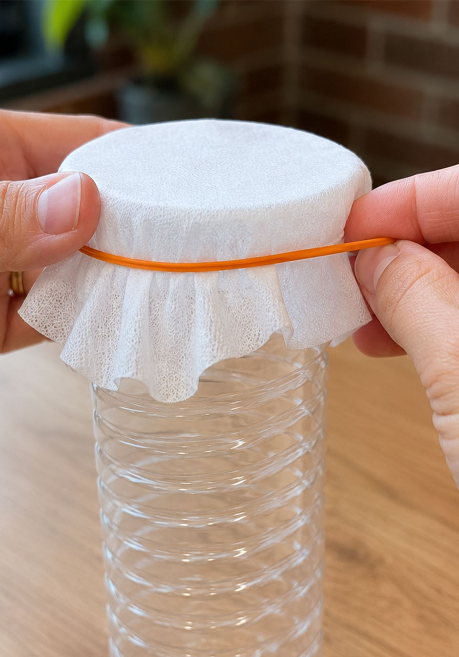 Covering bottle end with makeup wipe and rubber band for bubble snake experiment