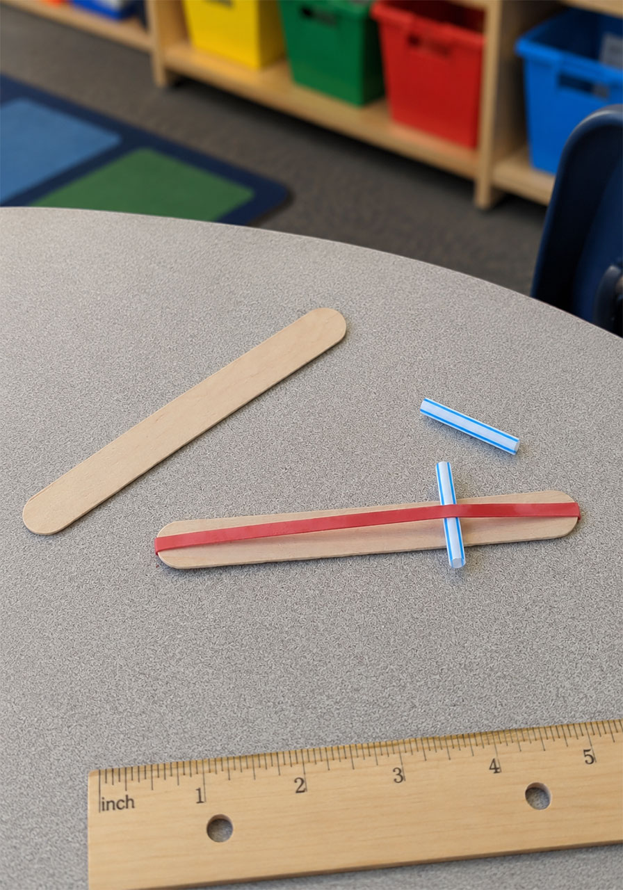 Placing a straw piece under the rubber band on a craft stick harmonica