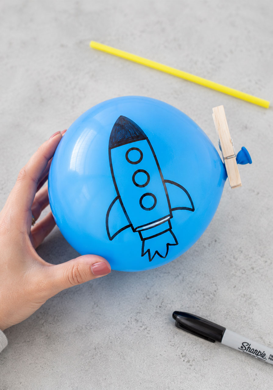 Child decorating an inflated balloon with a rocket ship design for a DIY STEM experiment