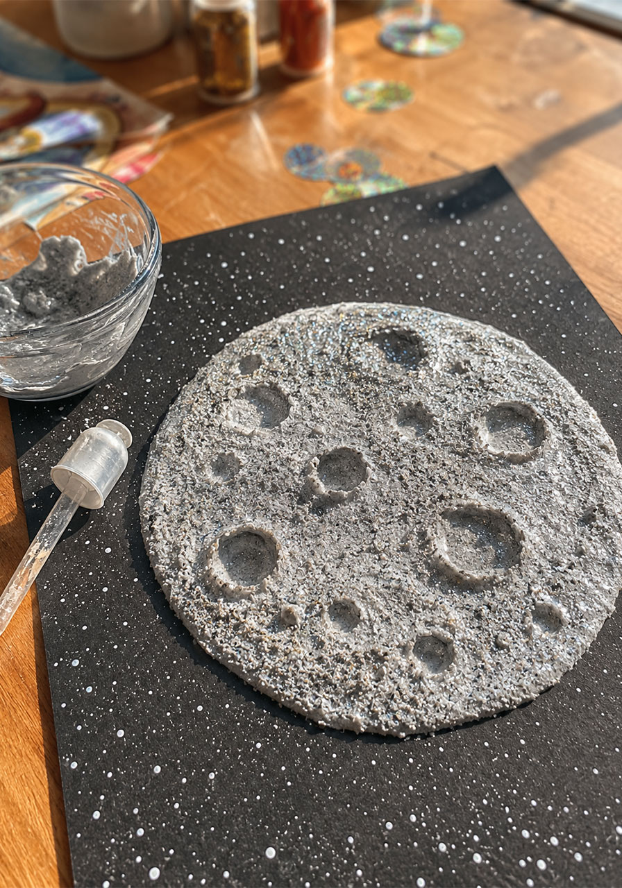 Finished DIY fizzing moon art project showing textured gray moon craft with glitter and craters