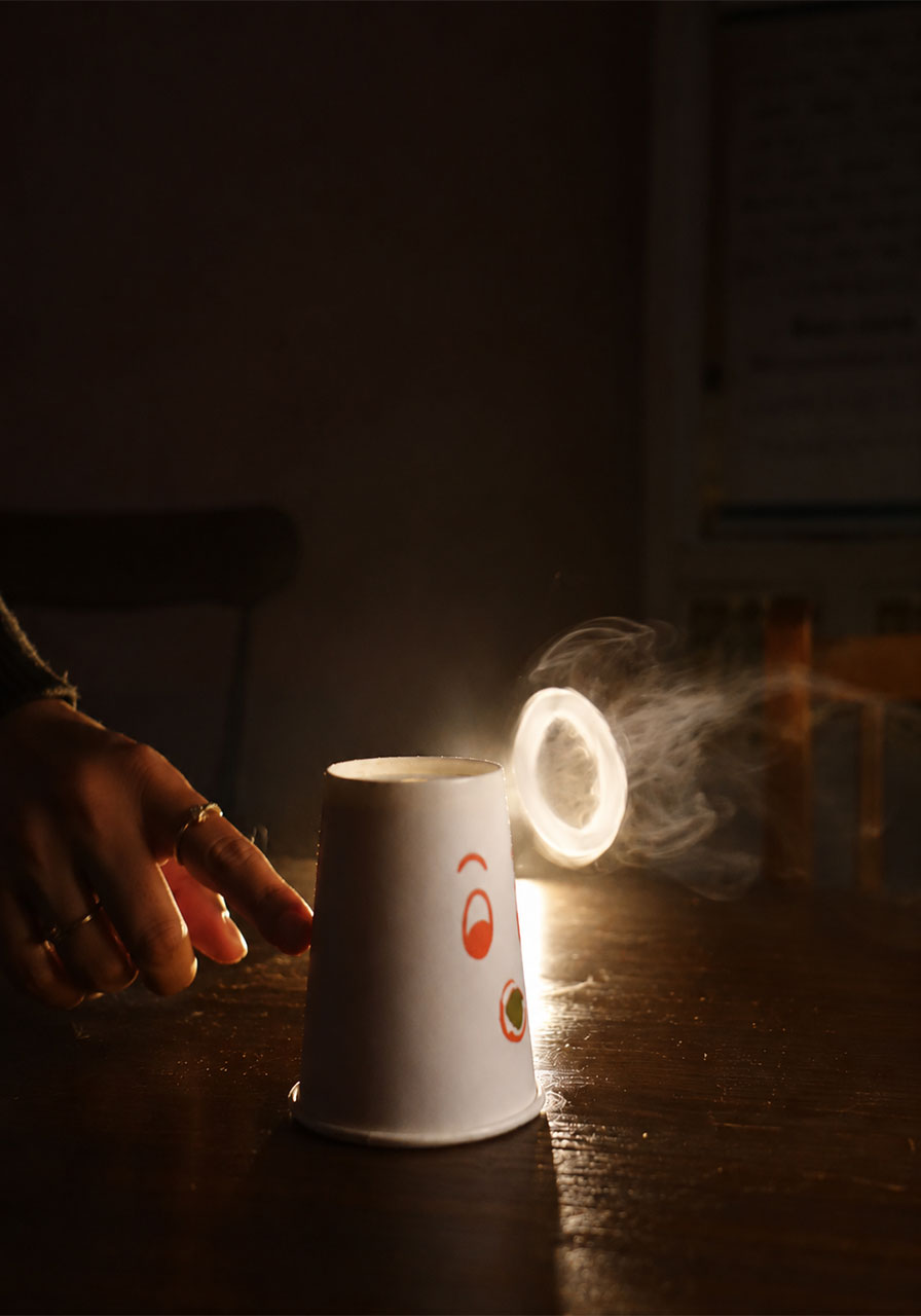 Glowing smoke ring floating above a DIY paper cup science experiment for kids
